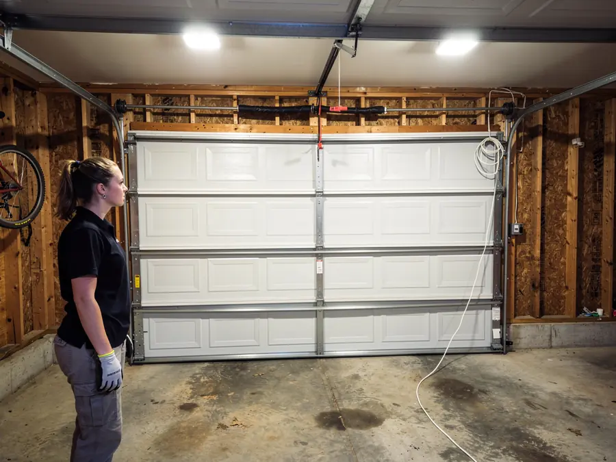 A technician stands in a garage looking at a white garage door.